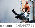 Friends, fun and shopping cart in outdoor for play, funny and bonding together in city for freedom. Women, town and adventure in trolley for comedy, laughing and crazy happiness in urban on weekend 143447711