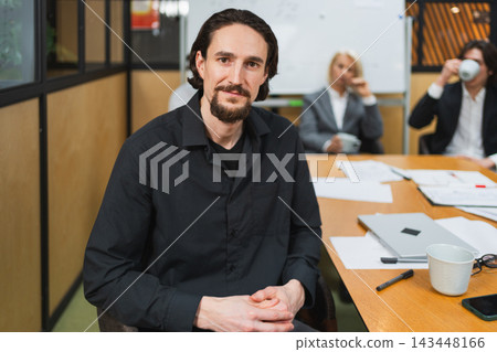 Portrait of team leader businessman in office, colleagues meeting in background. Confident business leader man sitting in office. Boss leader professional worker. Working process office life career Portrait of team leader businessman in office, colleagues meeting in background. Confident business leader man sitting in office. Boss leader professional worker. Working process office life career 143448166