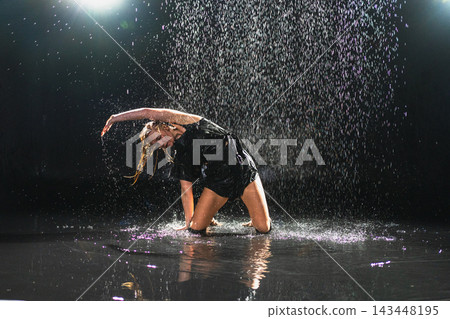 Contemporary woman dancer posing in rain water on black background. Female artist performer dancing with expression. Modern ballerina dancing in darkness. Passion dance in dark. Flexibility balance Contemporary woman dancer posing in rain water on black background. Female artist performer dancing with expression. Modern ballerina dancing in darkness. Passion dance in dark. Flexibility balance 143448195
