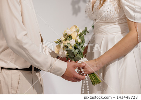 Groom holding bride's hand with bouquet of white flowers and pearls, wedding ceremony moment 143448728