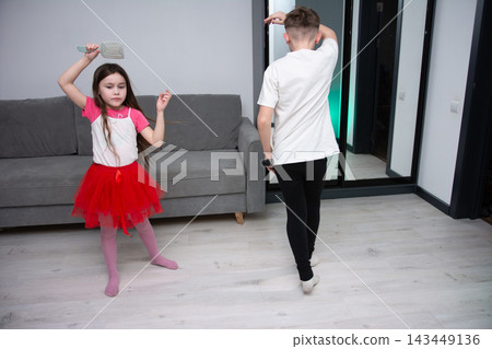 Kids enjoying dance and playtime in a cozy living room, showcasing creativity and energy with bright attire and joyful expressions in the evening hours Kids enjoying dance and playtime in a cozy living room, showcasing creativity and energy with bright attire and joyful expressions in the evening hours 143449136