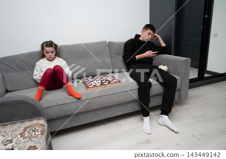 Two siblings engaging with technology and traditional games in a cozy modern living room during an evening at home Two siblings engaging with technology and traditional games in a cozy modern living room during an evening at home 143449142