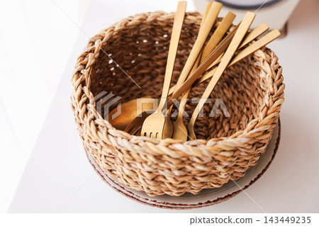 Golden utensils in a woven basket on a light surface by the window Golden utensils in a woven basket on a light surface by the window 143449235