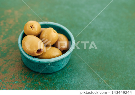 Green olives served in a blue bowl on a textured green surface for a simple and healthy snack Green olives served in a blue bowl on a textured green surface for a simple and healthy snack 143449244