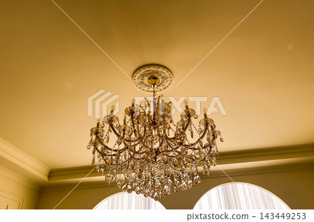 Elegant chandelier hangs from ceiling in bright room with soft lighting and gentle decor Elegant chandelier hangs from ceiling in bright room with soft lighting and gentle decor 143449253