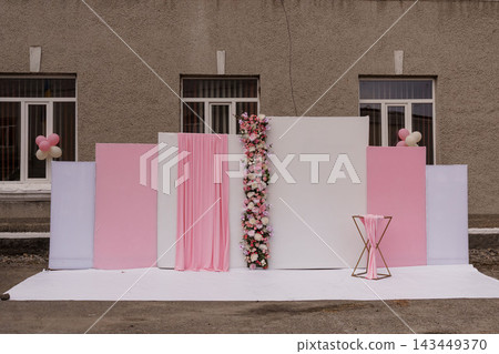 Outdoor pink and white floral backdrop with drapes and balloons against gray building wall. 143449370