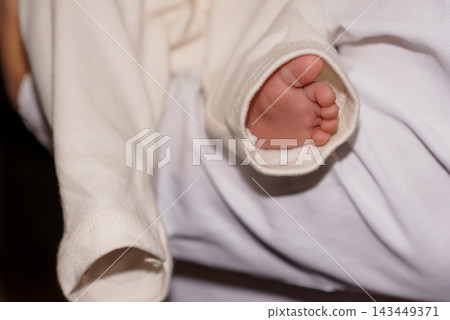 Tiny newborn foot peeking out from white clothing sleeve resting on soft fabric bedding background Tiny newborn foot peeking out from white clothing sleeve resting on soft fabric bedding background 143449371