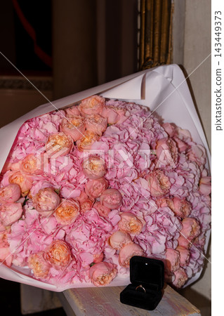 Massive pink rose bouquet wrapped in paper with a small open black ring box placed on wooden bench Massive pink rose bouquet wrapped in paper with a small open black ring box placed on wooden bench 143449373