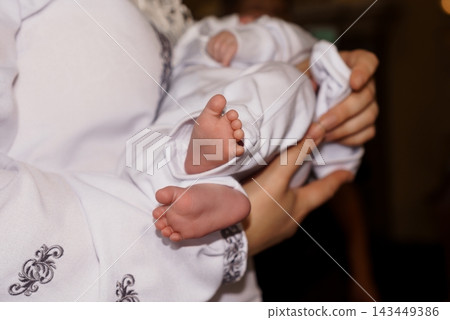 Close up of baby feet resting in mother's hands wrapped in white clothing showing new life and maternal love during quiet moments. 143449386