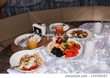 Romantic in-room dining table set with fresh fruit platter, juice, candlelight, and satin decor for hospitality use Romantic in-room dining table set with fresh fruit platter, juice, candlelight, and satin decor for hospitality use 143449387