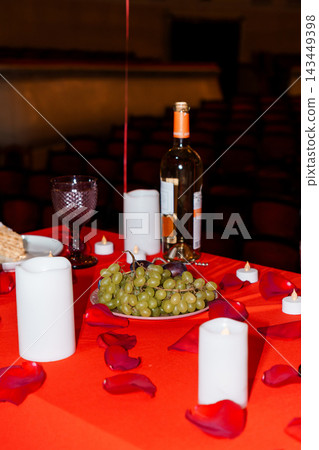 Romantic wine table setting with green grapes and red rose petals in candlelight theater environment Romantic wine table setting with green grapes and red rose petals in candlelight theater environment 143449398