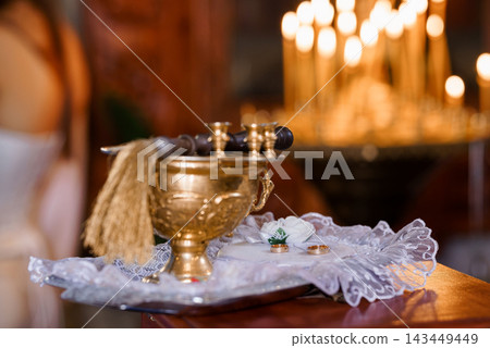 Gold Orthodox censer and wedding rings resting on lace doily in church with blurred candlelight background. Gold Orthodox censer and wedding rings resting on lace doily in church with blurred candlelight background. 143449449