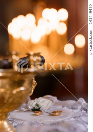 Golden wedding bands resting on an altar cross with glowing religious candles in the background. Golden wedding bands resting on an altar cross with glowing religious candles in the background. 143449450