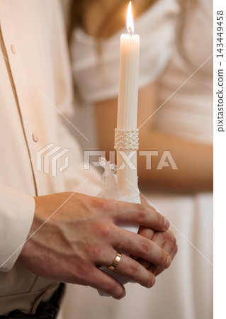 Hands holding lit candle with pearl detail at wedding ceremony closeup Hands holding lit candle with pearl detail at wedding ceremony closeup 143449458