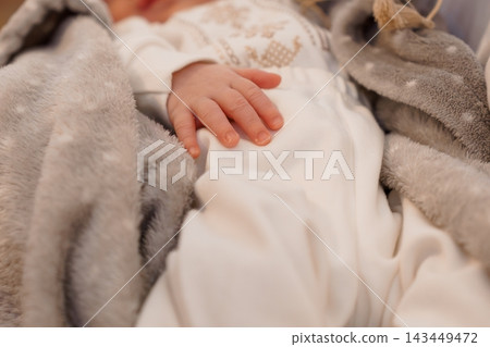 Baby hand resting on white soft cloth with gray fuzzy blanket in cozy warm indoor setting Baby hand resting on white soft cloth with gray fuzzy blanket in cozy warm indoor setting 143449472