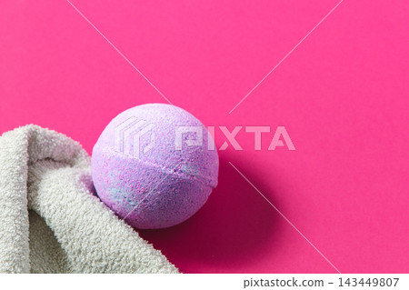 Bright pink background with a purple bath bomb and a towel nearby on a surface Bright pink background with a purple bath bomb and a towel nearby on a surface 143449807