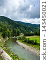 Scenic river flowing through lush green hills under a cloudy sky in early afternoon 143450021