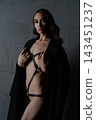 Woman in black leather harness and coat against dark concrete wall, dramatic studio lighting with moody atmosphere 143451237