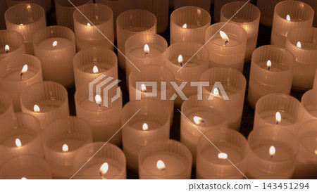A multitude of lit votive candles glowing in the darkness of a traditional church A multitude of lit votive candles glowing in the darkness of a traditional church 143451294