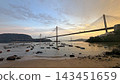 Suspension Hong Kong bridge spanning across a calm bay at sunset with small boats anchored near the shore 143451659