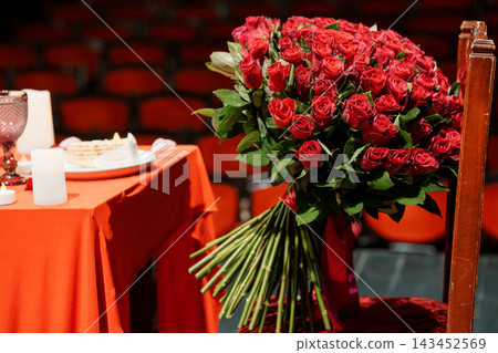 Large red rose bouquet on wooden chair with orange tablecloth in auditorium for romantic date setting 143452569