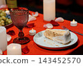 Romantic dessert table with wine glass slice of cake rose petals red cloth candlelight 143452570