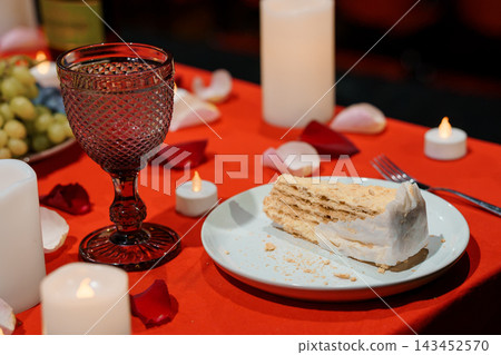 Romantic dessert table with wine glass slice of cake rose petals red cloth candlelight Romantic dessert table with wine glass slice of cake rose petals red cloth candlelight 143452570
