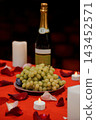 Green grapes on a plate with wine bottle and tealights on red tablecloth featuring scattered rose petals in romantic setting 143452571