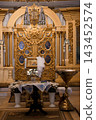 Gold reliquary altar with white flowers and holy water font in Catholic church sanctuary interior 143452574