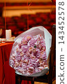 Large bouquet of dried pink roses wrapped in white paper resting on a theater chair with red background 143452578