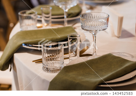 Elegant Formal Dinner Table Setting Featuring Crystal Glassware Green Napkins Gold Cutlery White Linens 143452583