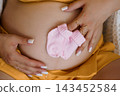 Pregnant belly with pink baby socks in hands showing gender reveal close up shot in warm yellow tones 143452584