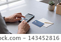 Person using a smartphone to complete a mobile payment at a desk with smartphone transaction technology purchase shopping business checkout contactless workspace convenience security 143452816