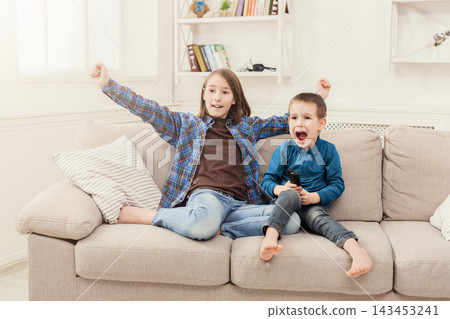 Happy children watching cartoon on tv at home, brother and sister having rest without parents, copy space Happy children watching cartoon on tv at home, brother and sister having rest without parents, copy space 143453241