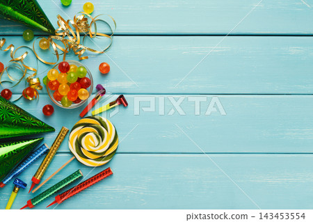 Carnival or party border of colorful hats and sweets, top view. Holiday decorations, lollipops and confetti on wooden planks, copy space for greeting, invitation or advertising. Birthday background Carnival or party border of colorful hats and sweets, top view. Holiday decorations, lollipops and confetti on wooden planks, copy space for greeting, invitation or advertising. Birthday background 143453554
