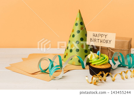 Delicious cupcake, gift and dotted cap on yellow background, copy space. Birthday, party, holiday concept Delicious cupcake, gift and dotted cap on yellow background, copy space. Birthday, party, holiday concept 143455244