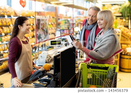 Smiling Caucasian Man And Woman Enjoying Shopping For Fresh Organic Fruits Together In Supermarket, Choosing Products From Shelves And Interacting With Store Employee, Business Concept. 143456379