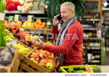 Happy Elderly Caucasian Man Choosing Fresh Fruits At Supermarket, Engaged In Phone Conversation While Shopping In Grocery Store, Enjoying Healthy Lifestyle. Weight Loss Concept. Happy Elderly Caucasian Man Choosing Fresh Fruits At Supermarket, Engaged In Phone Conversation While Shopping In Grocery Store, Enjoying Healthy Lifestyle. Weight Loss Concept. 143456399