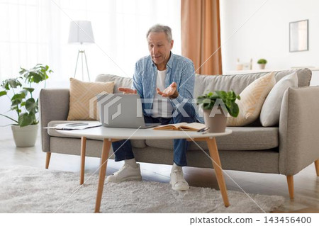 Happy Elderly Caucasian Man Smiling And Engaging In A Video Call While Sitting On Couch At Home. Enjoying Communication With Family Or Friends In A Comfortable Living Room Setting. Happy Elderly Caucasian Man Smiling And Engaging In A Video Call While Sitting On Couch At Home. Enjoying Communication With Family Or Friends In A Comfortable Living Room Setting. 143456400