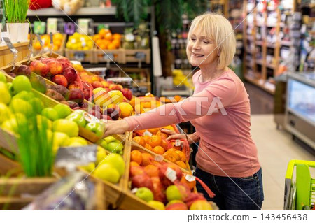 Smiling Elderly Caucasian Woman Selecting Fresh Fruits In Supermarket. Enjoying Shopping Experience While Choosing Organic Produce For A Healthy Diet In Grocery Store. Healthy Lifestyle Concept. Smiling Elderly Caucasian Woman Selecting Fresh Fruits In Supermarket. Enjoying Shopping Experience While Choosing Organic Produce For A Healthy Diet In Grocery Store. Healthy Lifestyle Concept. 143456438