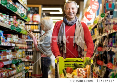 Smiling Elderly Caucasian Man Enjoying Shopping With Cart Full Of Fresh Vegetables In Supermarket, Filling Grocery List With Nutrient-rich Choices For Healthy Living. Weight Loss Concept. Smiling Elderly Caucasian Man Enjoying Shopping With Cart Full Of Fresh Vegetables In Supermarket, Filling Grocery List With Nutrient-rich Choices For Healthy Living. Weight Loss Concept. 143456547