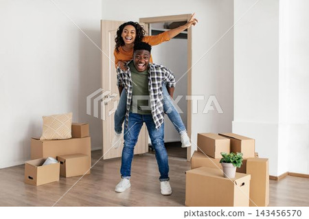 Smiling Black Couple Unpacking Boxes Together In Bright Apartment, Joyfully Celebrating Their New Home. Young Adults Filled With Excitement And Happiness In Modern Living Space. Home Concept. Smiling Black Couple Unpacking Boxes Together In Bright Apartment, Joyfully Celebrating Their New Home. Young Adults Filled With Excitement And Happiness In Modern Living Space. Home Concept. 143456570