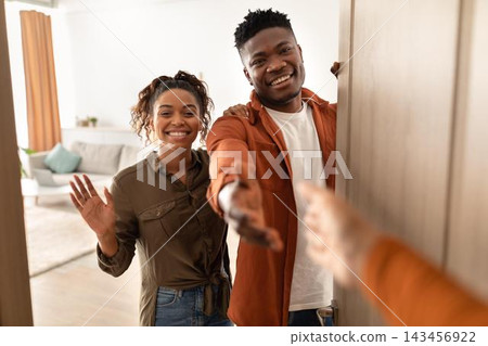 Smiling Black Young Couple Welcoming Guests With Open Arms And Friendly Gestures At Home, Enjoying A Warm Interaction In Their Living Room. Happiness And Hospitality Concept. Smiling Black Young Couple Welcoming Guests With Open Arms And Friendly Gestures At Home, Enjoying A Warm Interaction In Their Living Room. Happiness And Hospitality Concept. 143456922