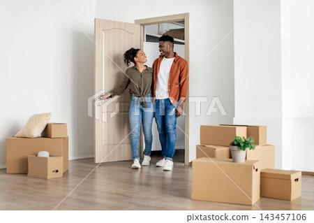 Smiling Young African American Couple Embracing While Moving Into New Home, Holding Door Open With Cardboard Boxes Surrounding In Bright, Modern Indoor Space. Exciting New Beginning Concept. Smiling Young African American Couple Embracing While Moving Into New Home, Holding Door Open With Cardboard Boxes Surrounding In Bright, Modern Indoor Space. Exciting New Beginning Concept. 143457106