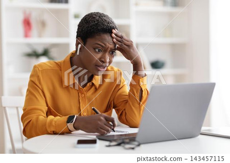 Worried Black Female Professional Expressing Concern While Working On Laptop At Home Office, Taking Notes. Displaying Emotion Of Frustration And Stress At Her Workplace, Home Office Concept. Worried Black Female Professional Expressing Concern While Working On Laptop At Home Office, Taking Notes. Displaying Emotion Of Frustration And Stress At Her Workplace, Home Office Concept. 143457115