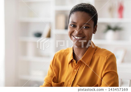 Smiling Black Woman In Professional Setting, Sitting At Desk In Office, Engaged And Confident, As She Works. A Positive Mood Demonstrating Professionalism And Determination. Business Concept. 143457169