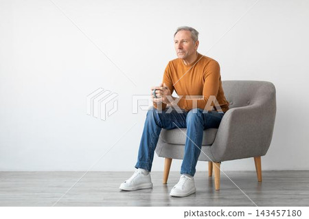 Thoughtful Elderly Caucasian Man Sitting On Comfortable Chair With Coffee In Hands, Reflecting On Life In Cozy Indoor Setting, Enjoying Moment Of Relaxation And Peace. Thoughtful Elderly Caucasian Man Sitting On Comfortable Chair With Coffee In Hands, Reflecting On Life In Cozy Indoor Setting, Enjoying Moment Of Relaxation And Peace. 143457180