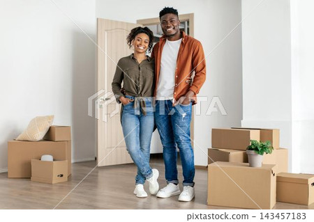 Smiling Young African American Couple Standing Together In New Apartment Amongst Moving Boxes, Displaying Emotion Of Happiness, Feeling Excited About Moving In Together. Home Concept. Smiling Young African American Couple Standing Together In New Apartment Amongst Moving Boxes, Displaying Emotion Of Happiness, Feeling Excited About Moving In Together. Home Concept. 143457183
