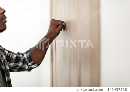 Unrecognizable Black Male Knocking On Door With His Fist. The Image Captures A Sense Of Anticipation And Expectation In A Modern Indoor Setting. Concept Of Arrival Or Visit. Unrecognizable Black Male Knocking On Door With His Fist. The Image Captures A Sense Of Anticipation And Expectation In A Modern Indoor Setting. Concept Of Arrival Or Visit. 143457238