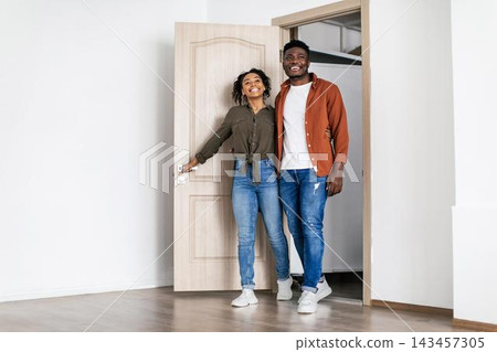 Smiling Black Couple Standing Together At Home Entrance, Embracing New Beginnings, Feeling Happy And Excited About Their New Living Space, Indoor Setting, Home Lifestyle Concept. Smiling Black Couple Standing Together At Home Entrance, Embracing New Beginnings, Feeling Happy And Excited About Their New Living Space, Indoor Setting, Home Lifestyle Concept. 143457305
